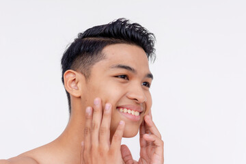 A happy young asian man looking happy while feeling his smooth, clean shaven cheeks and face. Isolated on a white backdrop.