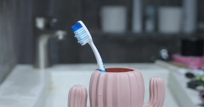 Male hand puts toothbrush in cactus-shaped cup. After brushing teeth, man puts toothbrush in toothbrush cup, turns off tap water, and starts day refreshed and washed. Wet male hand. Selective focus