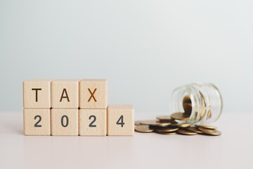 Tax 2024 text on wooden cube block with blurred coins and jar for income tax return.Tax,...