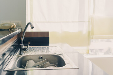 Dirty and unwashed dishes are stacked in stainless steel kitchen sink. Unwashed ceramic cups,...