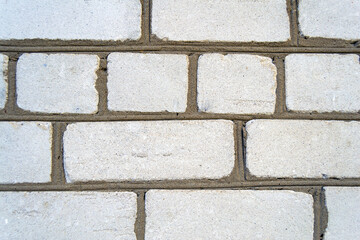 An image of the texture of a brick wall with a coarse-grained, embossed surface. Small cracks and cement inclusions. Horizontal image.