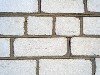 An image of the texture of a brick wall with a coarse-grained, embossed surface. Small cracks and cement inclusions. Horizontal image.