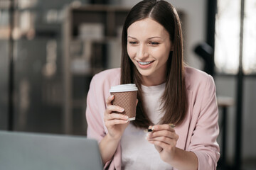 businesswoman sits in a office working on laptop and enjoys a coffee.