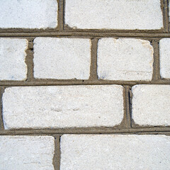 An image of the texture of a brick wall with a coarse-grained, embossed surface. Small cracks and cement inclusions. Square image.