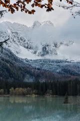Papier Peint photo Lavable Forêt dans le brouillard Amazing winter scenery with lake under snowy mountain peaks covered with mist and clouds