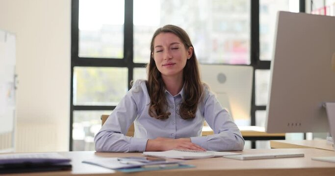 Portrait of young serious and strict female worker sitting in office at table shaking head