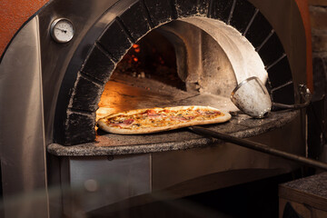 A stone oven radiates warmth as a chef retrieves a pizza adorned with melting cheese and rich...