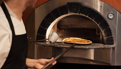 A chef skillfully slides a pizza into a wood-fired oven, showcasing the blend of tradition and...