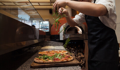 A chef delicately scatters fresh arugula over a gourmet pizza, adding a touch of green to the...