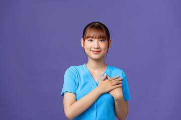 Cheerful woman smiling and holding hands on chest isolated over purple wall