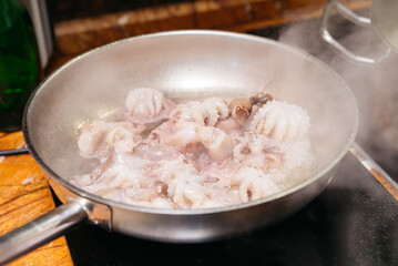 Boiling Baby Octopus in Stainless Steel Skillet. A stainless steel skillet on the stove with boiling water and baby octopus, a step in the preparation of a seafood dish.