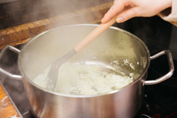 Sauteing Onions in a Stainless Steel Saucepan. A chef sautes diced onions in a stainless steel saucepan over a stove, the beginning steps of a flavorful meal preparation.
