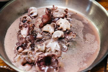Cooking Baby Octopus in Stainless Steel Pot. Fresh baby octopus simmering in a broth within a stainless steel pot, a preparation step in a gourmet seafood recipe.