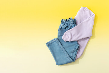 Children's lilac sweater and folded jeans on a yellow background. Stylish children's clothes. Copy space