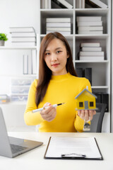 Fototapeta na wymiar House model near an Asian female sales representative offering prices and conditions of purchase or rental on a table in a new location. In choosing real estate in her office