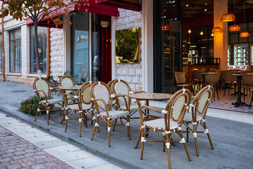 Fototapeta na wymiar Street view of a coffee terrace with tables and chairs. Free cafe table. Outdoor empty coffee and restaurant terrace