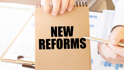 Text NEW REFORMS on brown paper notepad in businessman hands on the table with diagram. Business...