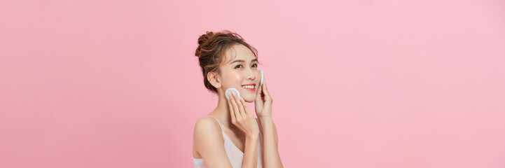 Attractive beauty young asian woman clean skin with cotton pad removing make up on pink background.