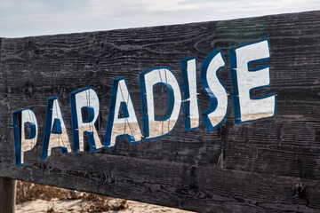 Inscription "paradise" on wooden board on sea beach closeup on seaside background