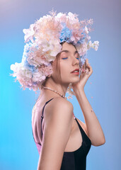 portrait of a beautiful woman with clear skin and colored makeup, wearing a flower wreath on a blue background. Spring beauty