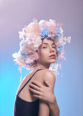 portrait of a beautiful woman with clear skin and colored makeup, wearing a flower wreath on a blue background. Spring beauty