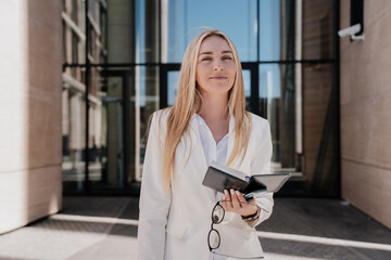 Smiling businesswoman in chic attire enjoys a sunny day while holding a planner