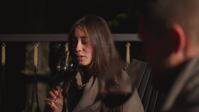Woman tastes wine with friend on night terrace. Young couple spends first romantic date in cozy restaurant. Pretty lady rests with boyfriend