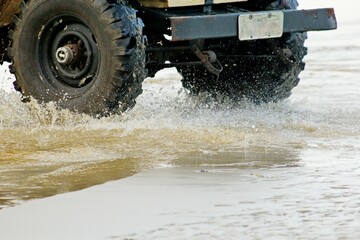 Large black tires crsooing stream. Splashing water from wet sand. 