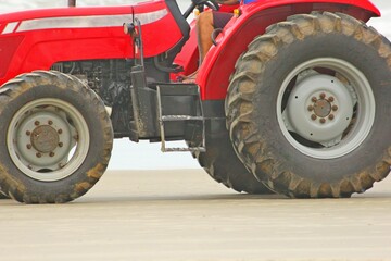 Close up of red tractor with large black tires standing on the sand