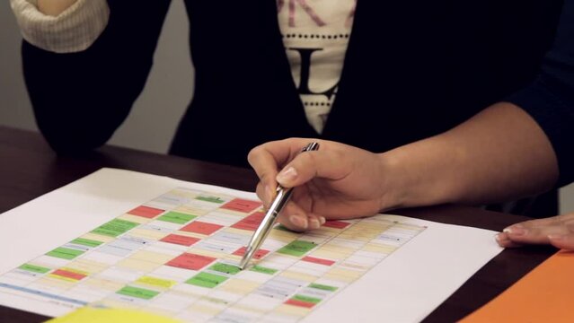 Steadicam Close up Shot of Two Women Discussing Project Timeline Actively With Pens Poking At A Printed Table