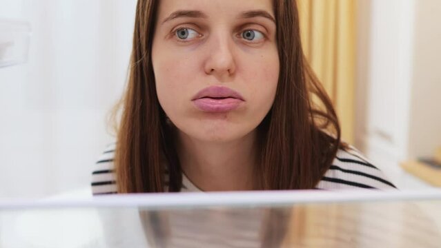 View from refrigerator of sad woman opening her empty fridge with no groceries looking inside with sad expressing being hungry has no food and products for cooking