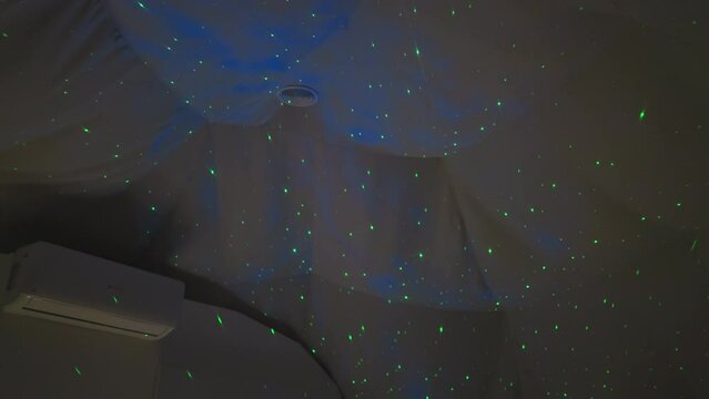 Double bed in glamping house with green lights on ceiling. Nightlight with projector that lights up room with green dots for quiet sleep