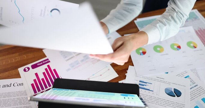 Woman studies data on digital tablet with graphs and documents closeup. Financial report and marketing with analytics
