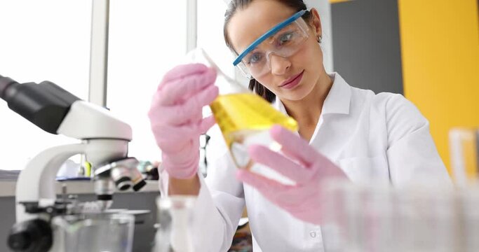 Doctor in protective glasses holds test tube with a yellow liquid in laboratory closeup. Laboratory diagnostics oil research concept