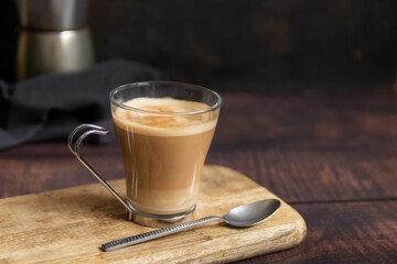 Cup of coffee with milk and teaspoon and Italian coffee pot in the background