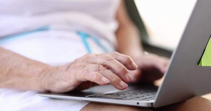 Hands of elderly woman are typing on laptop keyboard. Searching for information on the Internet for elderly concept