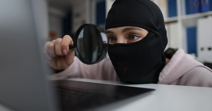 Internet theft and persons in balaclava with magnifying glass behind laptop. Internet intellectual property theft concept