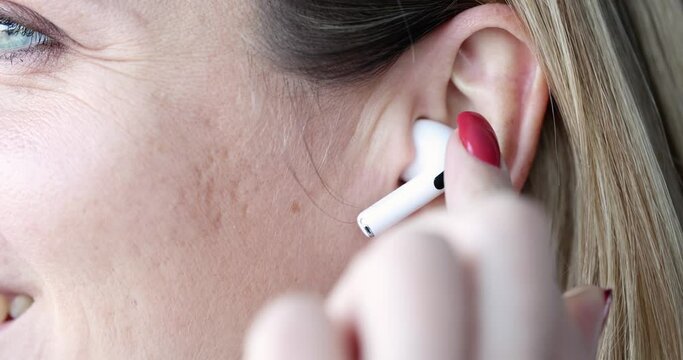 Woman inserts white wireless earpiece into ear. Listening to music or talking concept
