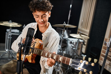 adorable talented jolly teenager in casual outfit playing his guitar and smiling happily in studio