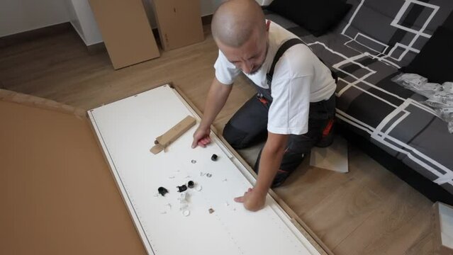 a man is watching how to assemble furniture with his own hands. A male craftsman in a work suit looks at the details and thinks about how to assemble a cabinet . High quality FullHD footage