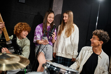 cheerful cute teenage girls singing and smiling while boys playing guitar and drums in studio