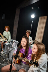 cheerful pretty teenagers singing and playing various instruments in studio, musical group