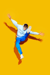 Fototapeta na wymiar Trendy fashion in motion. Person jumps with flair, dressed stylish sportswear, shows pop of excitement against bright yellow background. Concept of beauty, trends, modern style, shopping, sales.
