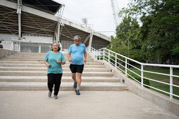 Happy and smile couples elderly asian running on stairs for workout, jogging on morning, senior exercise outdoors for good healthy. Concept of healthcare and active lifestyle for healthy