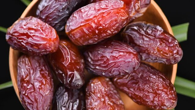 Dates fruit. Date fruits with palm tree leaf, in a wooden bowl, rotating on black background. Medjool dates close up. Top view