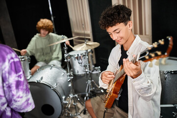 focus on cheerful cute teenage boy playing guitar actively next to his blurred band members