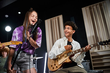 Fototapeta premium cheerful talented teenagers in casual outfits singing and playing guitars while in their studio