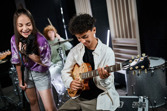 cheerful cute teenage girl singing next to her cute friend playing guitar and other boy on drums