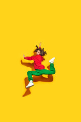 Fototapeta na wymiar Fashion takes flight. Young happy woman, student dressed in trendy, modern sportwear and hat jumping in motion against yellow background. Concept of fashion and beauty, modern style, shopping, sales.