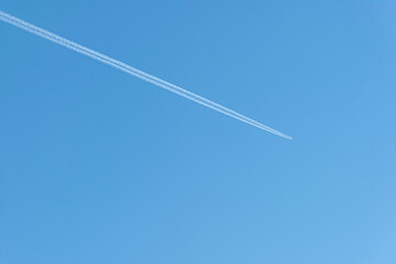 airplane flying across a bright blue sky with a contrail minimalist background
